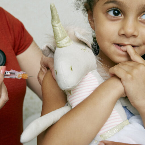 Happy young girl about to receive a vaccine from a medical professional